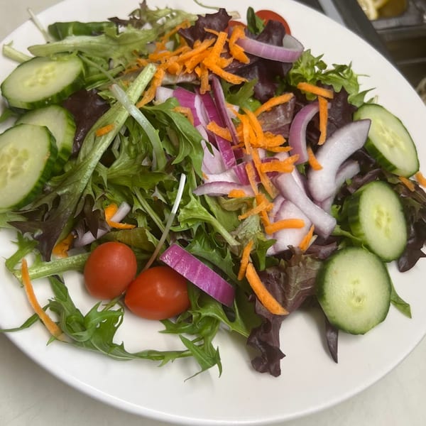 Fresh garden salad with mixed greens, sliced cucumbers, cherry tomatoes, red onions, and shredded carrots.