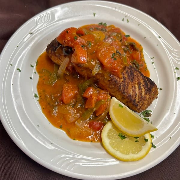 Grilled fish topped with a vibrant tomato and vegetable sauce, garnished with lemon wedges and parsley.