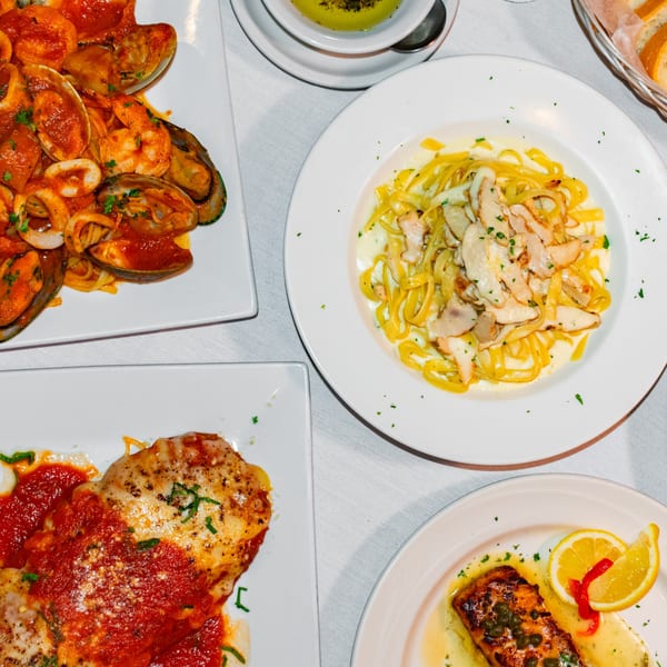 A table laden with Bella Pasta's Italian dishes, including seafood pasta, chicken alfredo, and salmon.