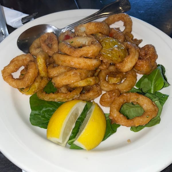 Fried calamari rings with lemon wedges and spinach on a white plate at Bella Pasta.