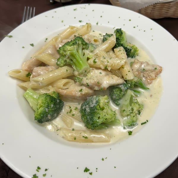 Creamy penne pasta with chicken, broccoli, and parsley on a white plate at Bella Pasta.